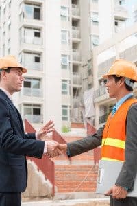 A Businessman and Construction Worker Shaking Hands in Front of Commercial Property Site