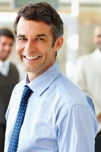 Middle-Aged Businessman Smiling at the Camera and Standing in Front of Other Businessmen