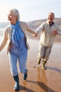 Retired Couple Holding Hands, Smiling, and Running on a Beach