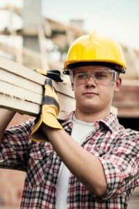 Construction worker carrying several boards on his shoulder.