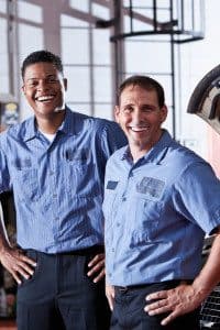 Two Body Repair Shop Employees Smiling and Standing in a Garage with their Hands on their Hips
