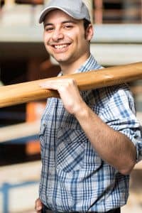 Male Contractor Carrying Lumber and Smiling at the Camera