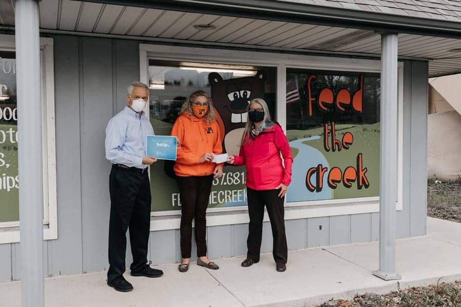 people in masks outside insurance agency donating a check