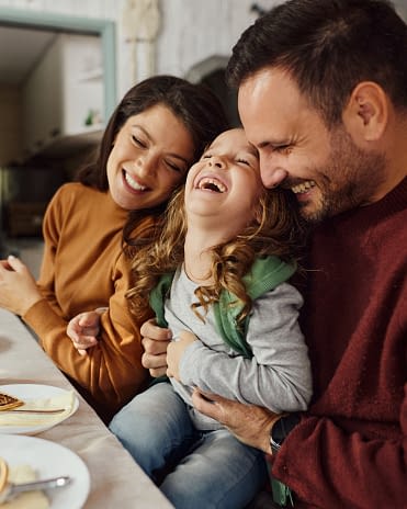 Happy parents having fun with their small girl during lunch at dining table.