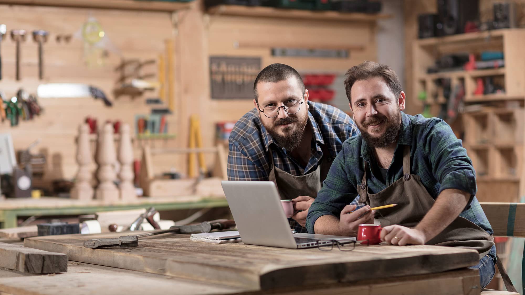 Employer and employee in wood shop looking at laptop.