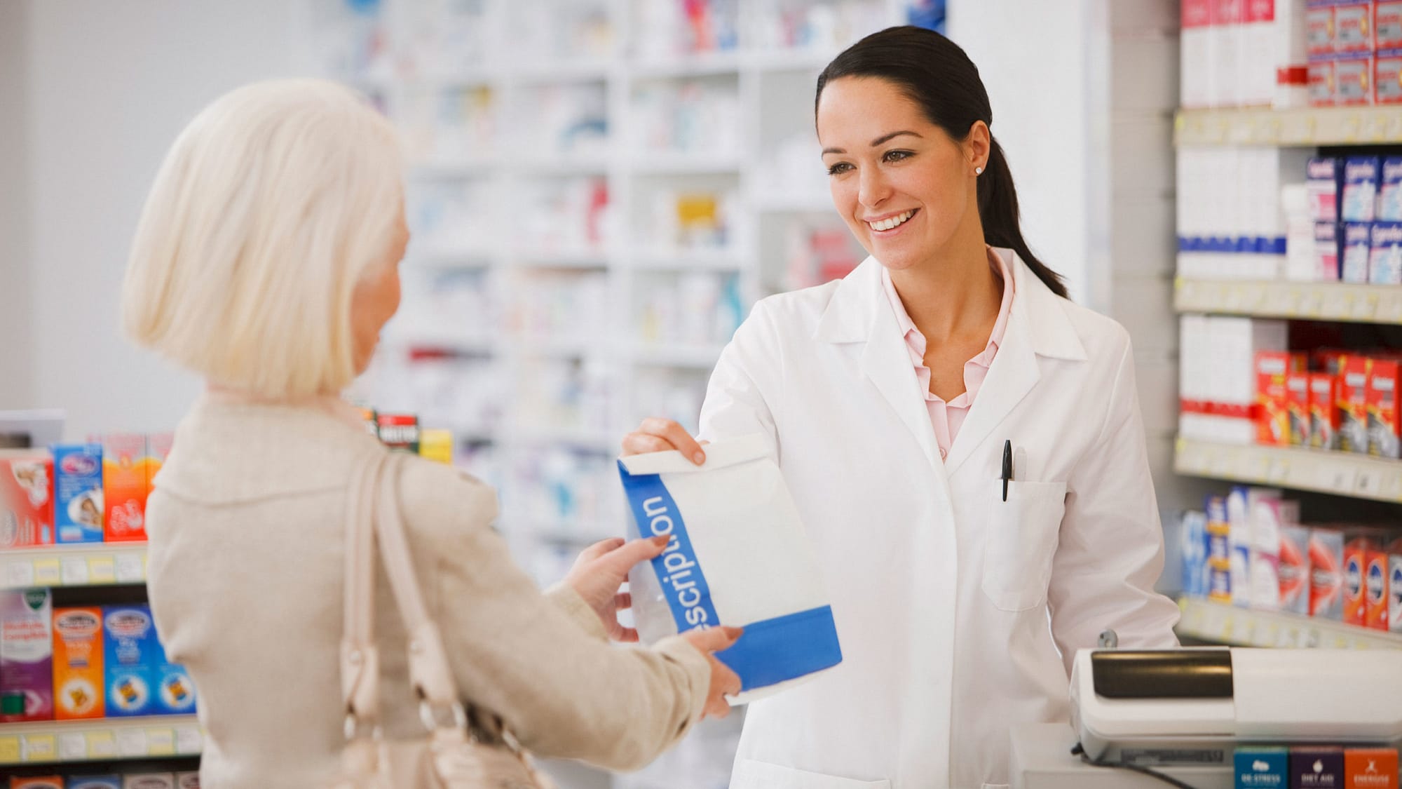Pharmacist handing customer a prescription in a drug store.