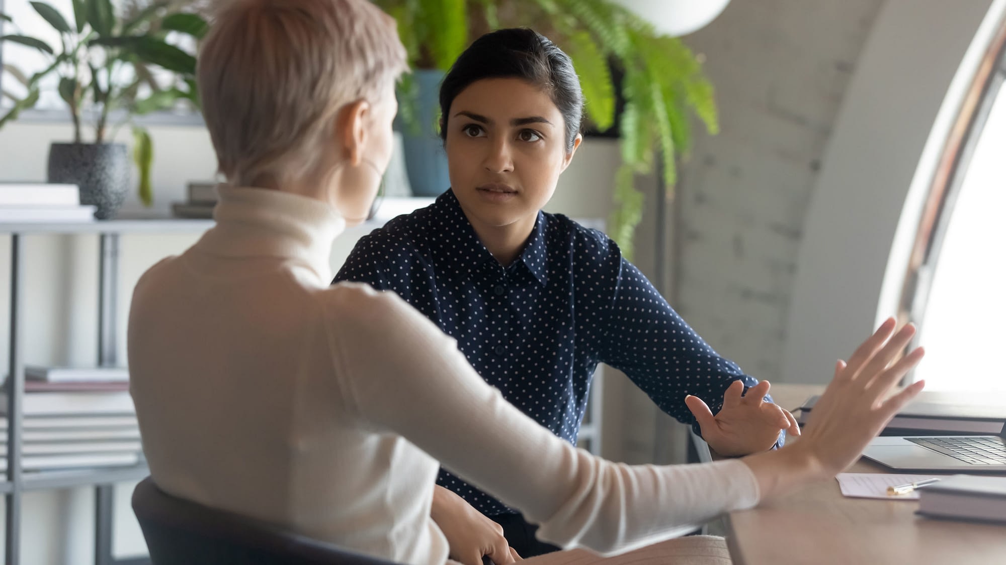 Two females having a conversation at a table.