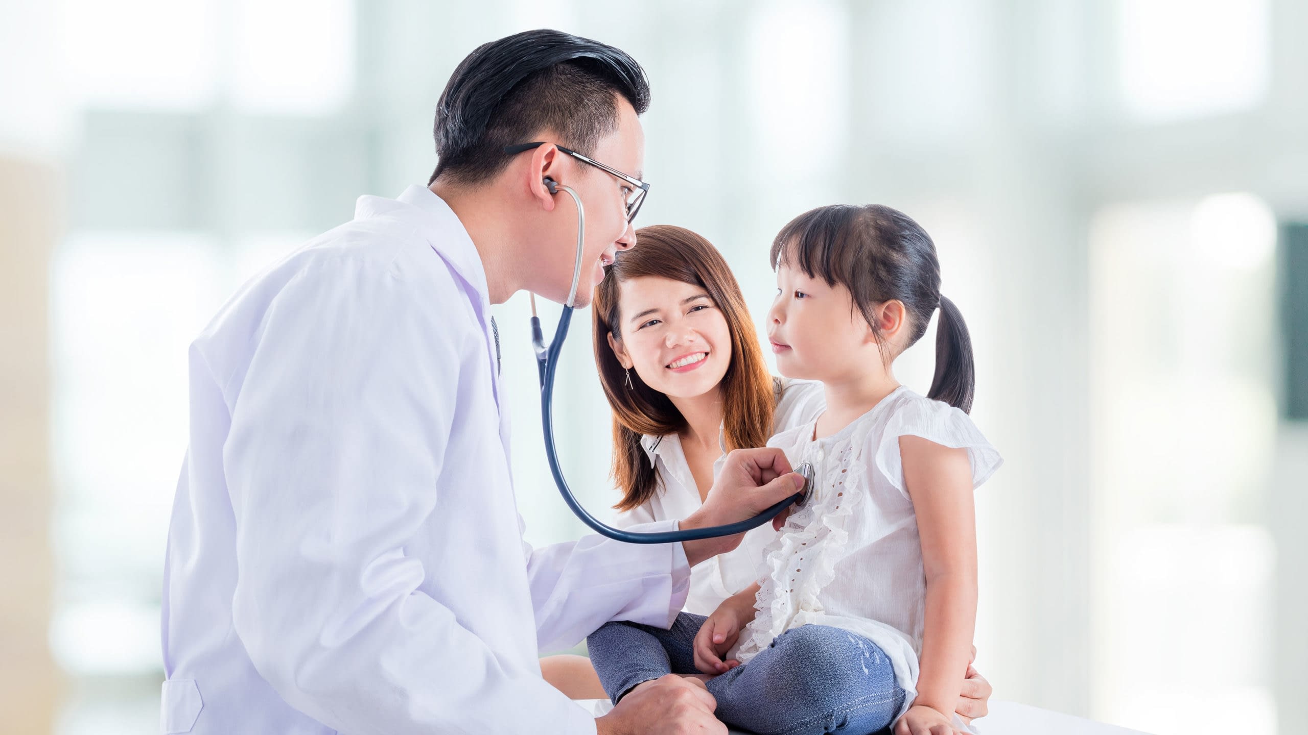 Doctor listening to young girl's breathing with mother next to her.
