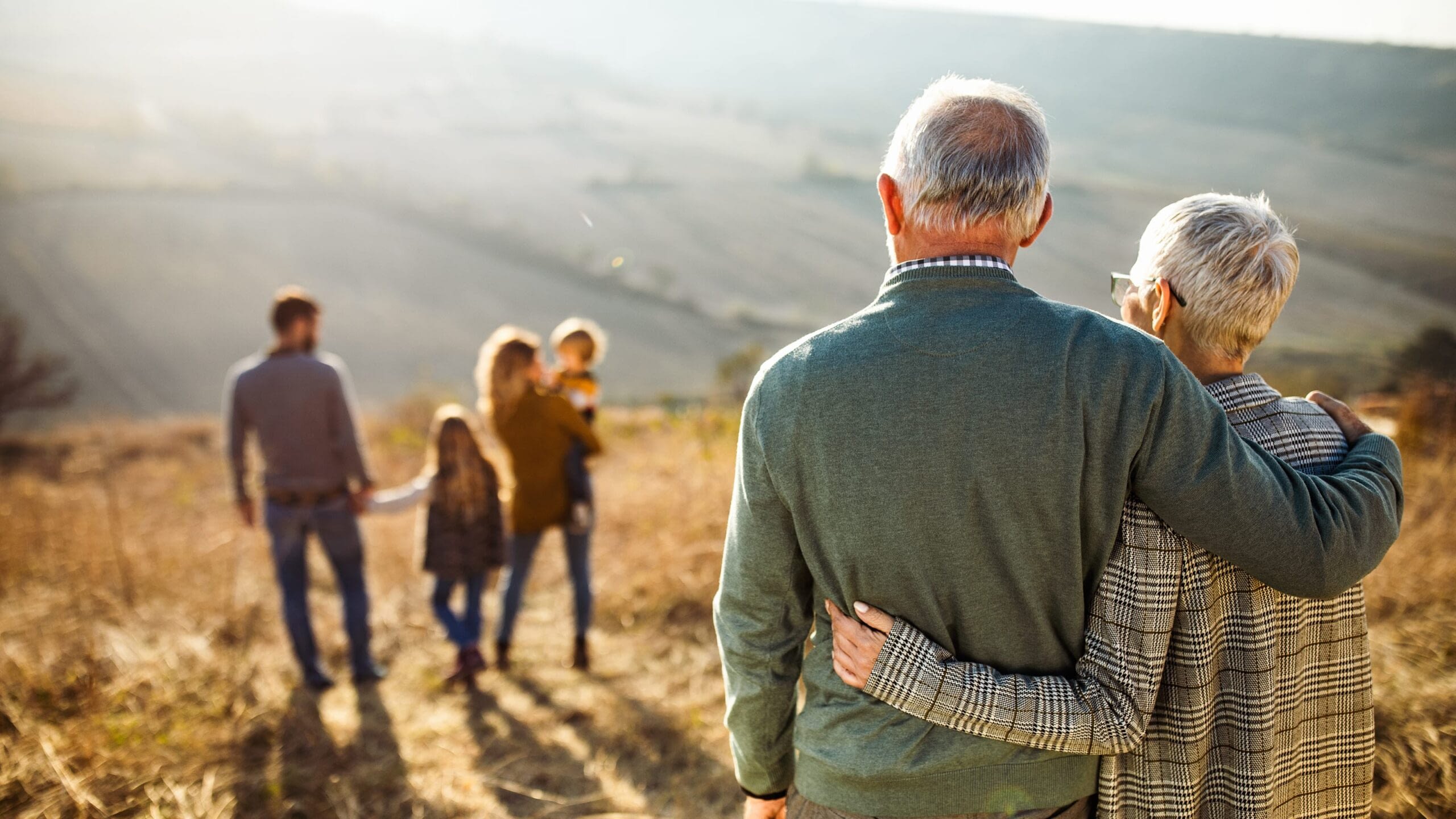 Senior couple hugging and watching as their adult children walk away with their two children.