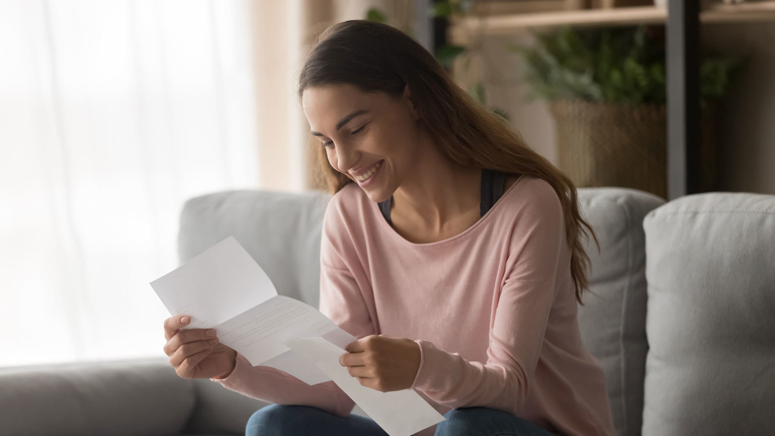 Young woman sitting on sofa reading health reimbursement arrangement letter.