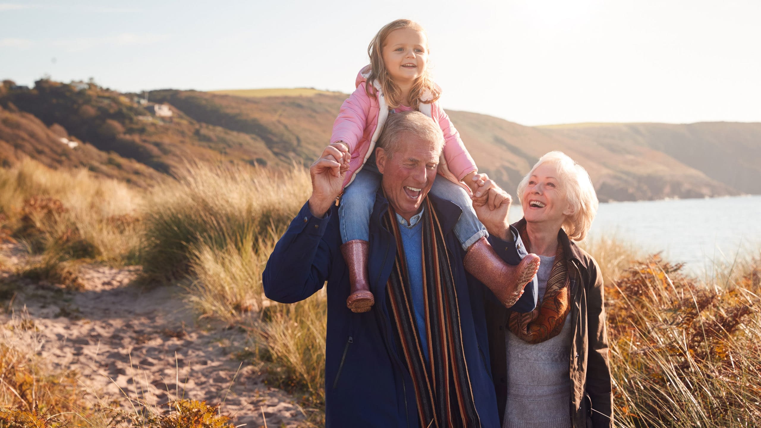 Grandfather giving granddaughter a ride on his shoulders while walking on a trail with her grandmother.