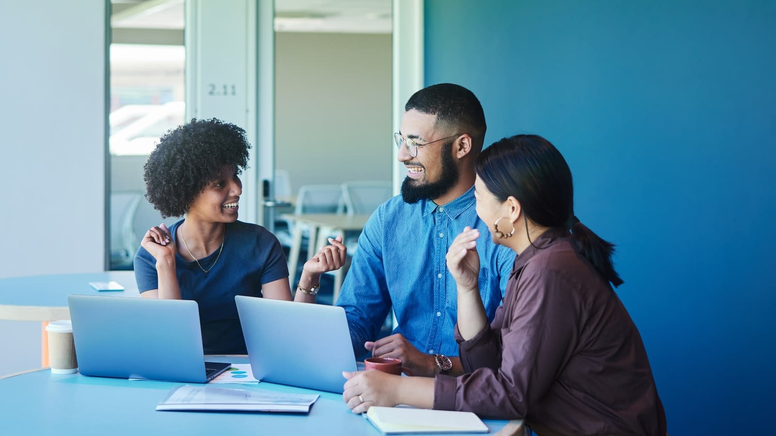 cybersecurity three coworkers working on laptops and talking to one another