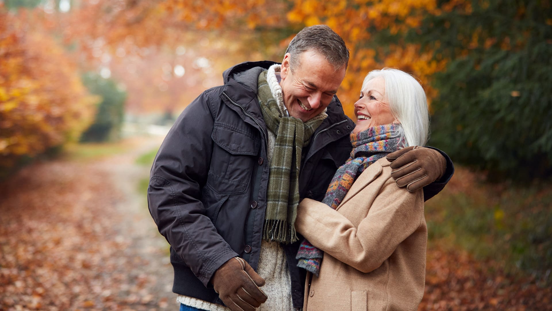 Senior couple embracing while walking on a woodland path in the Autumn.