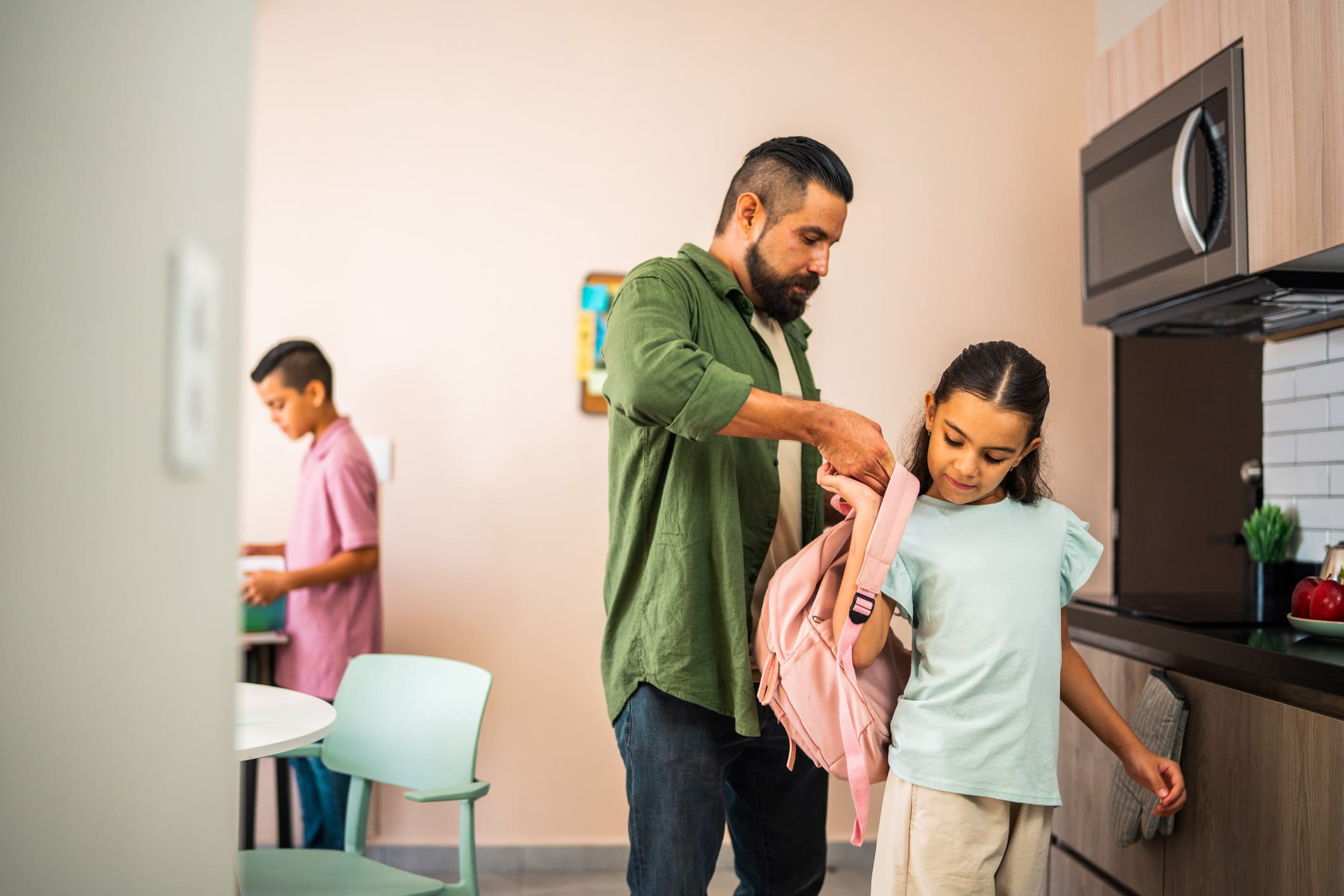Daughter and father preparing bag for first day of school at home Father helps daughter put on a backpack.
