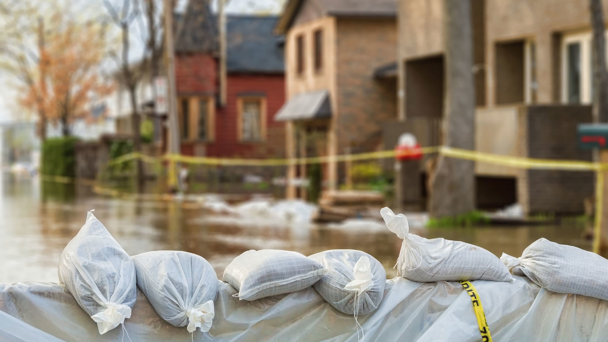 Sandbags lining the street with flooded homes in the background.