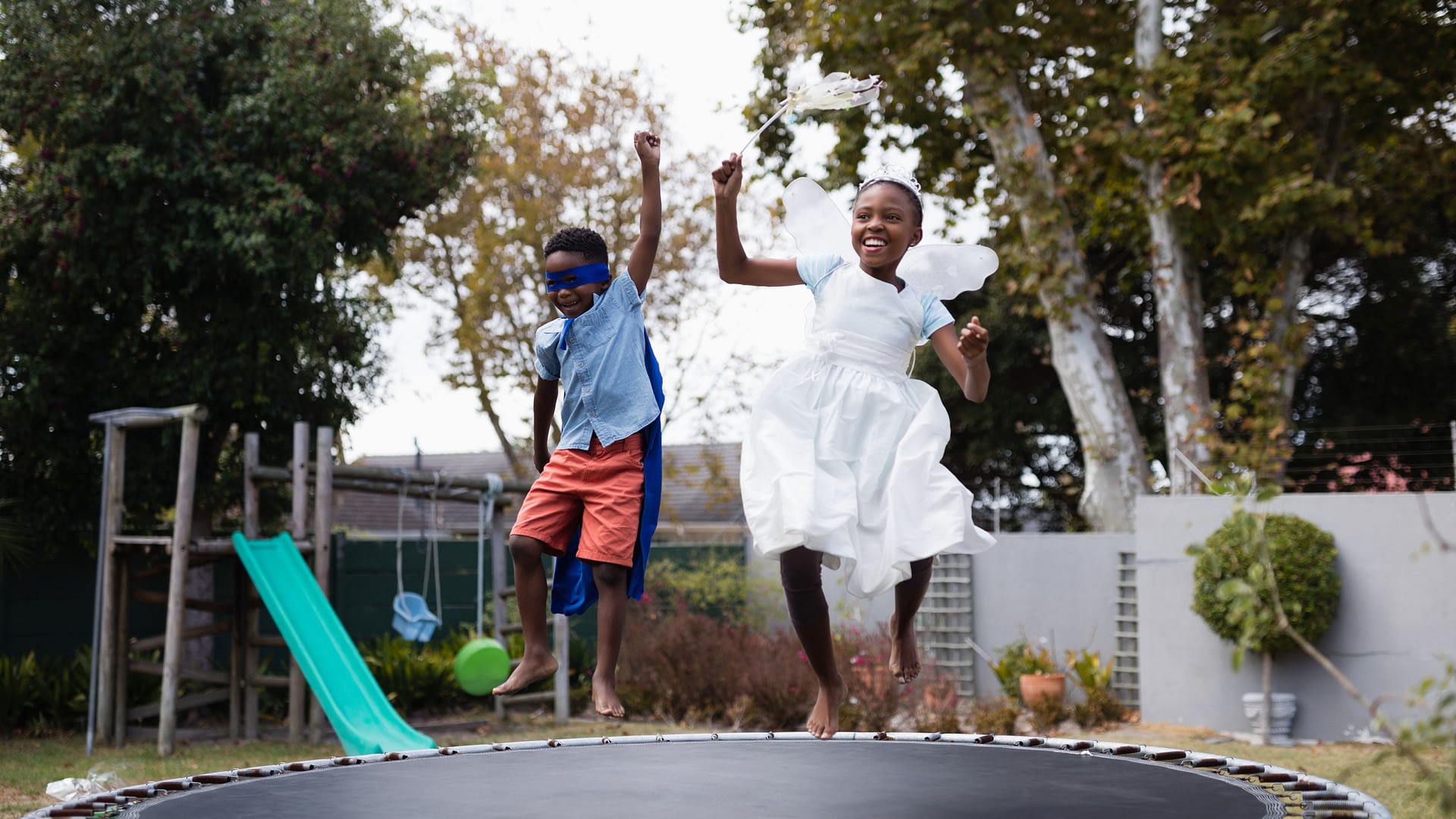 Kids jumping on a trampoline in the backyard of a residence.