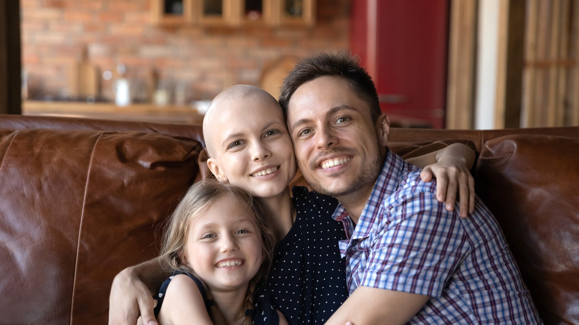 Mother undergoing cancer treatment hugging her husband and daughter.