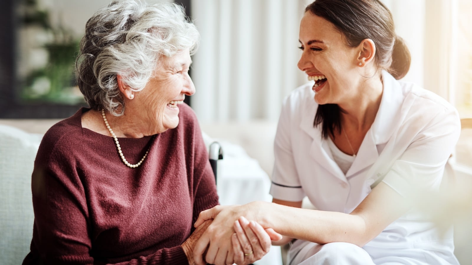 elderly woman and caregiver laughing and holding hands