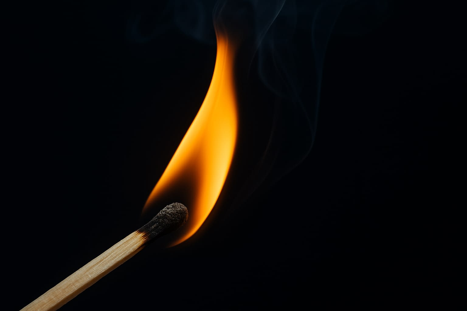 Close-up of Burning Match for Fire Prevention Awareness A close-up photo of a lit wooden match with a bright orange flame and dark background symbolizing fire safety awareness
