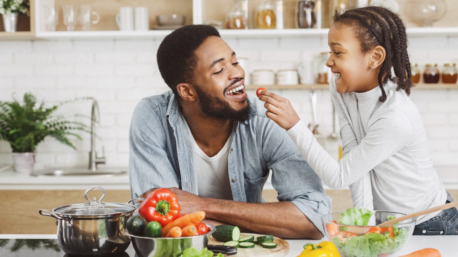 Food For Dehydration Cute african girl giving her dad cherry tomato while cooking