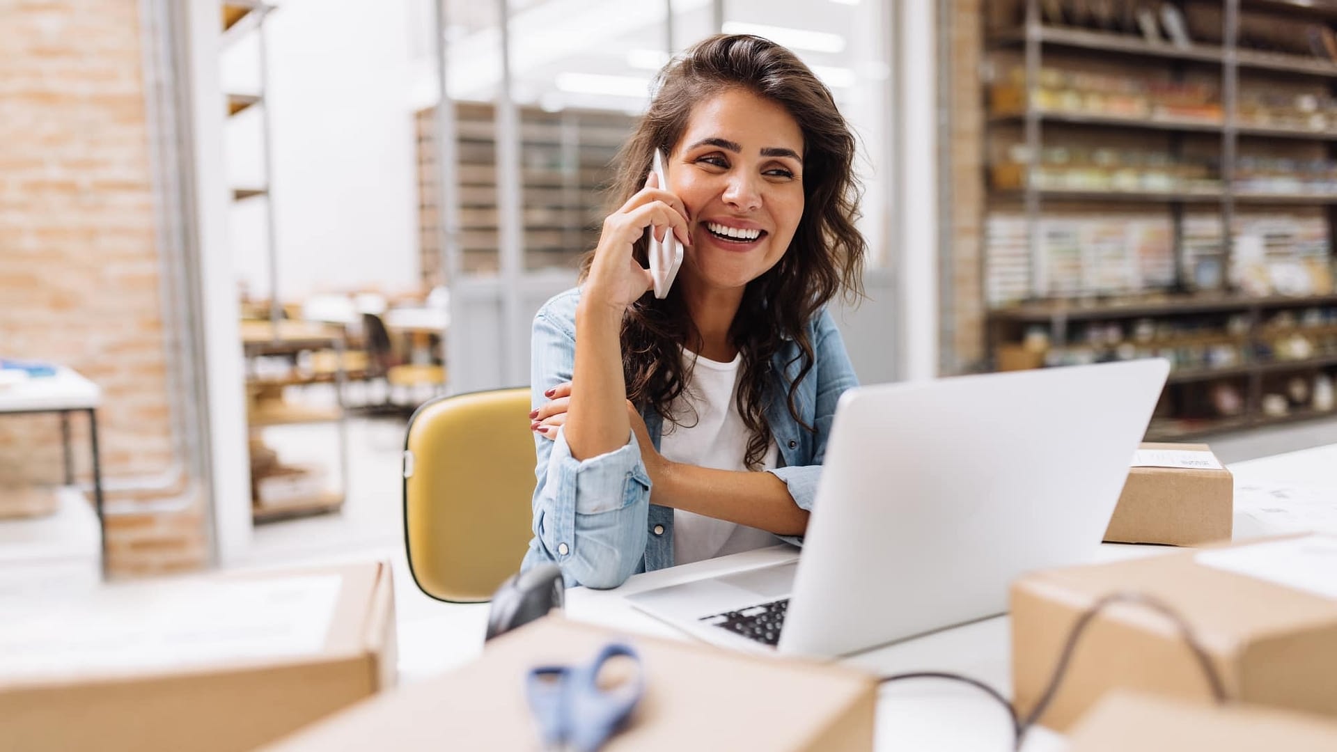 A smiling woman talking on the phone while looking at her laptop