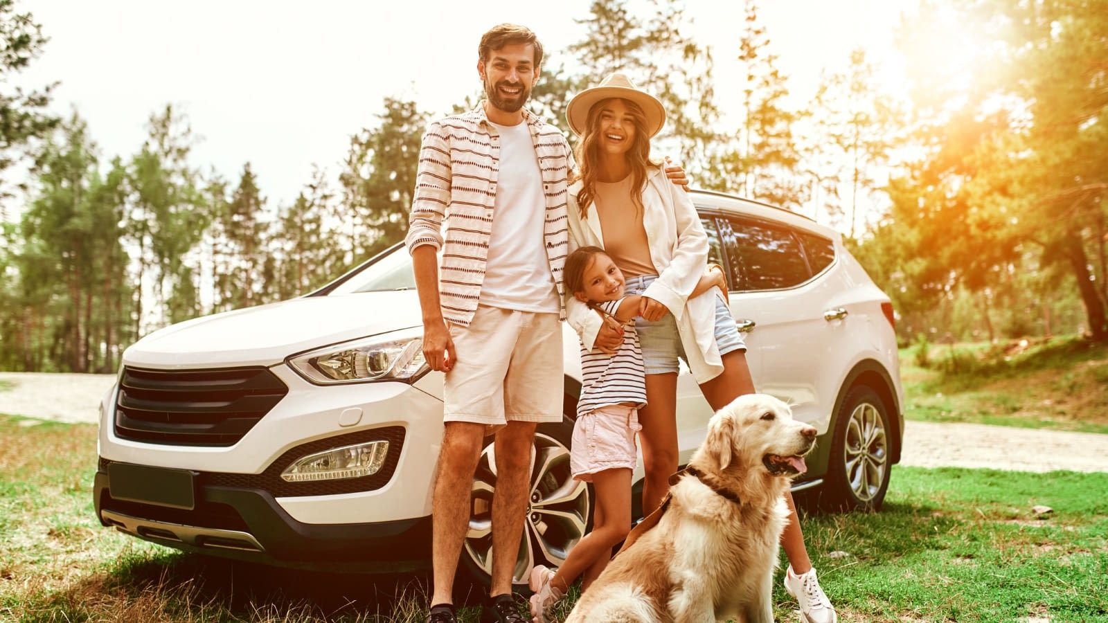 family in front of car smiling with dog