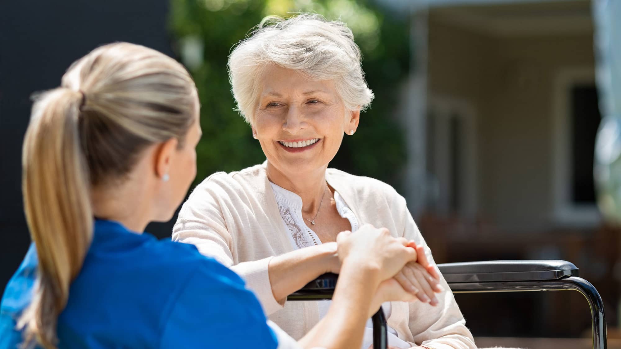 Nurse talking to an elderly patient sitting in a wheelchair outside.