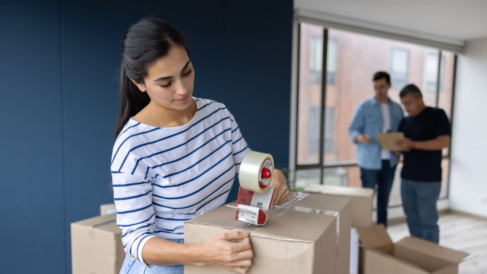 moving woman packing up boxes while two men discuss paperwork