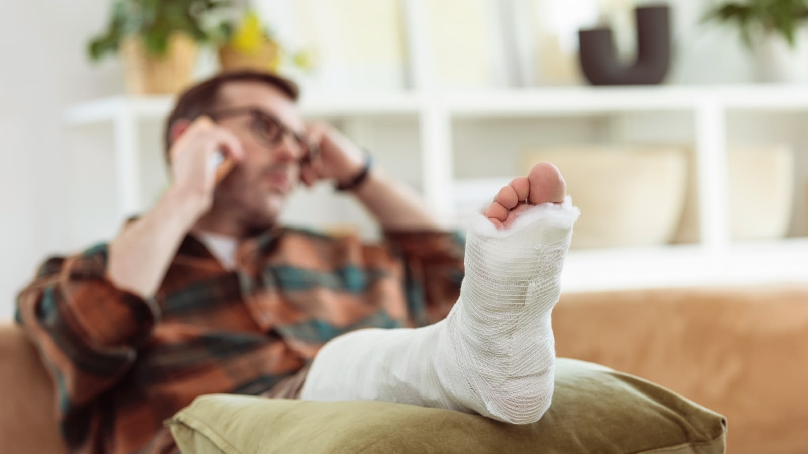 man with broken foot laying on couch talking on the phone