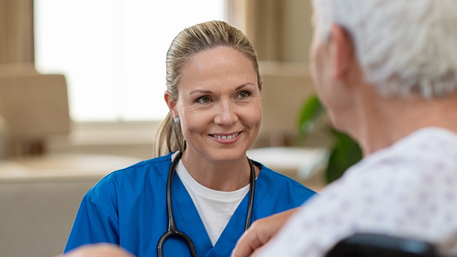 Nurse chatting with a senior woman sitting in a wheelchair.