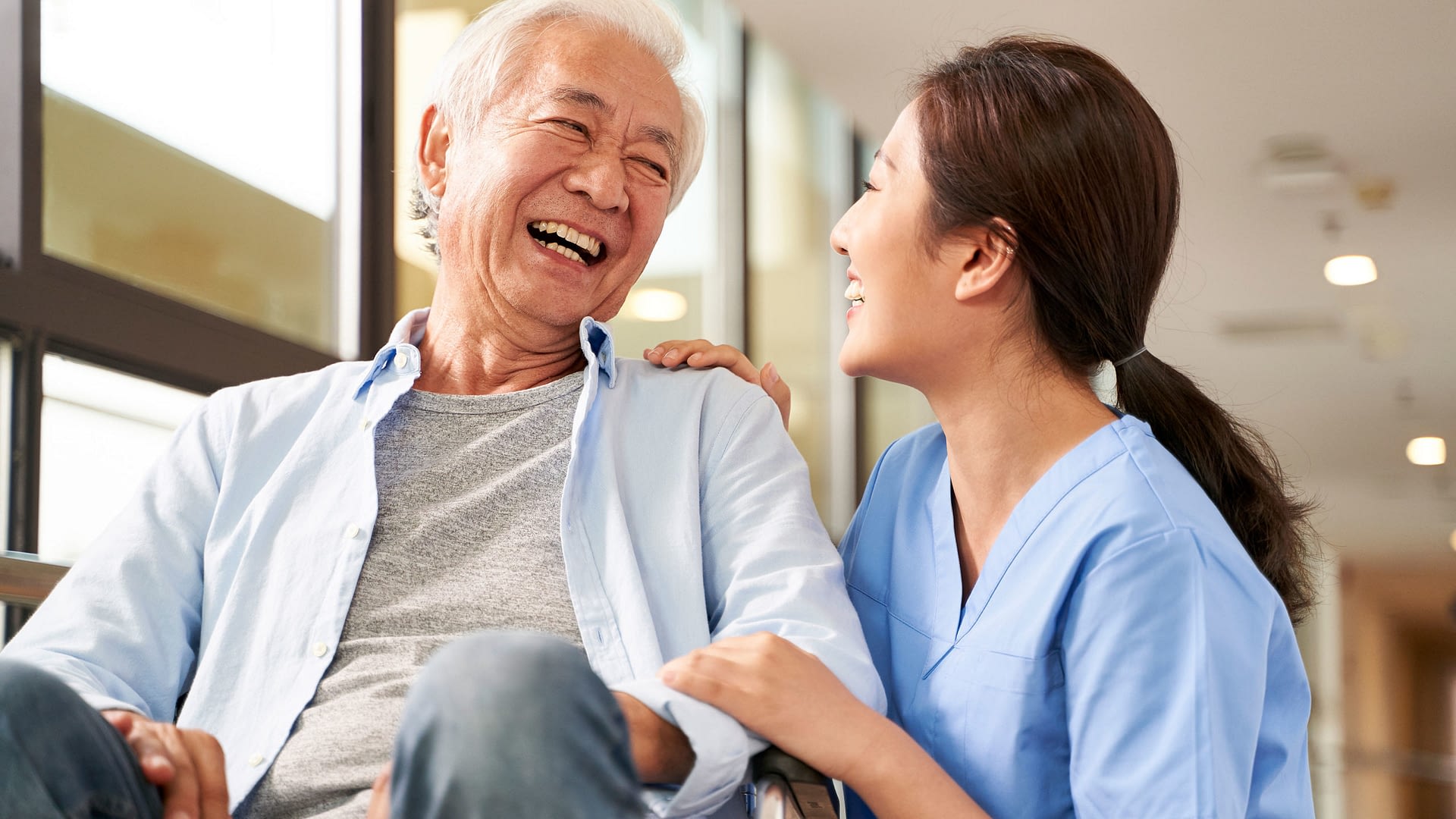 Nurse laughing with senior patient sitting in wheelchair.