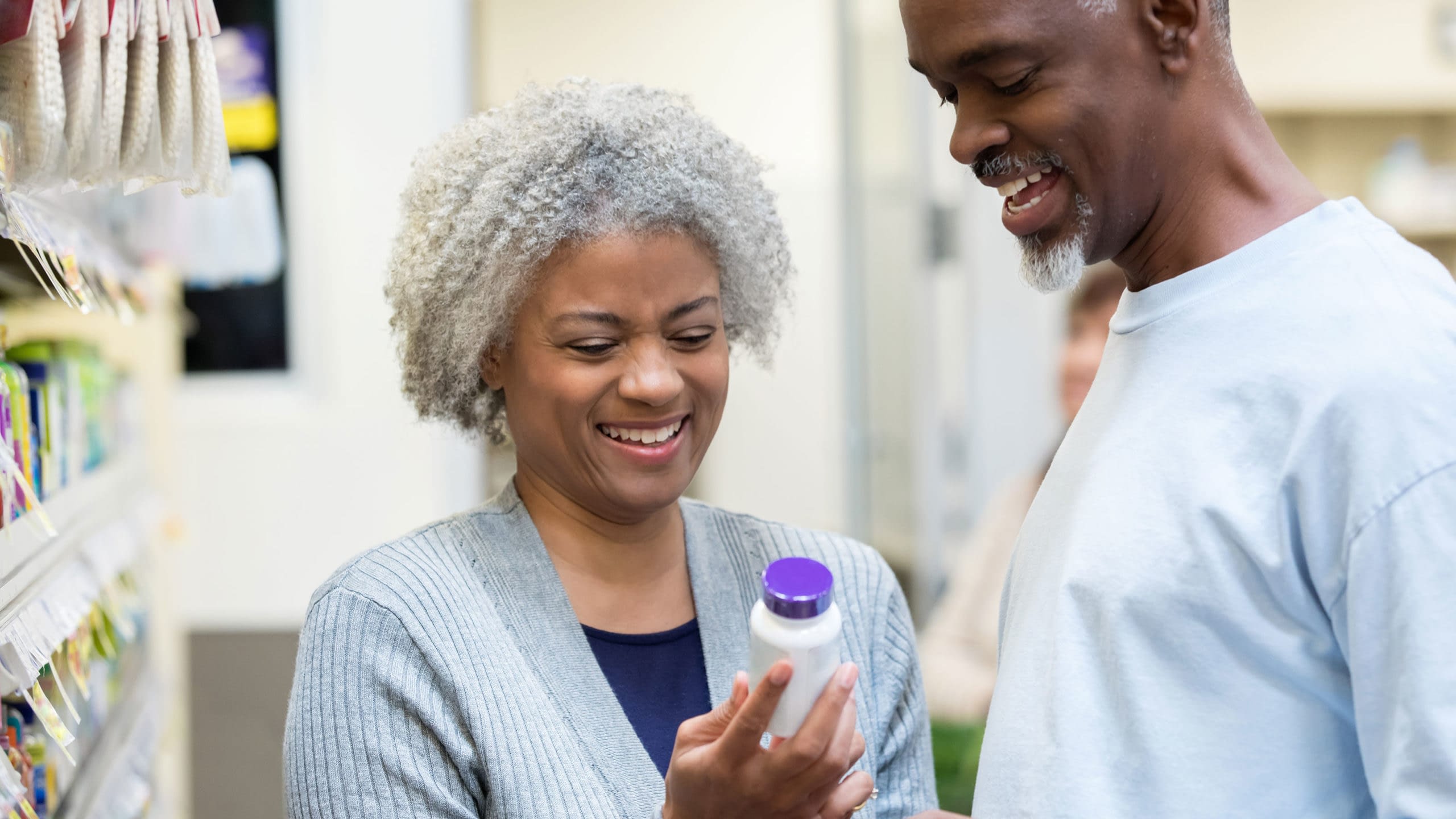 Senior couple reading medicine bottle labels in pharmacy.