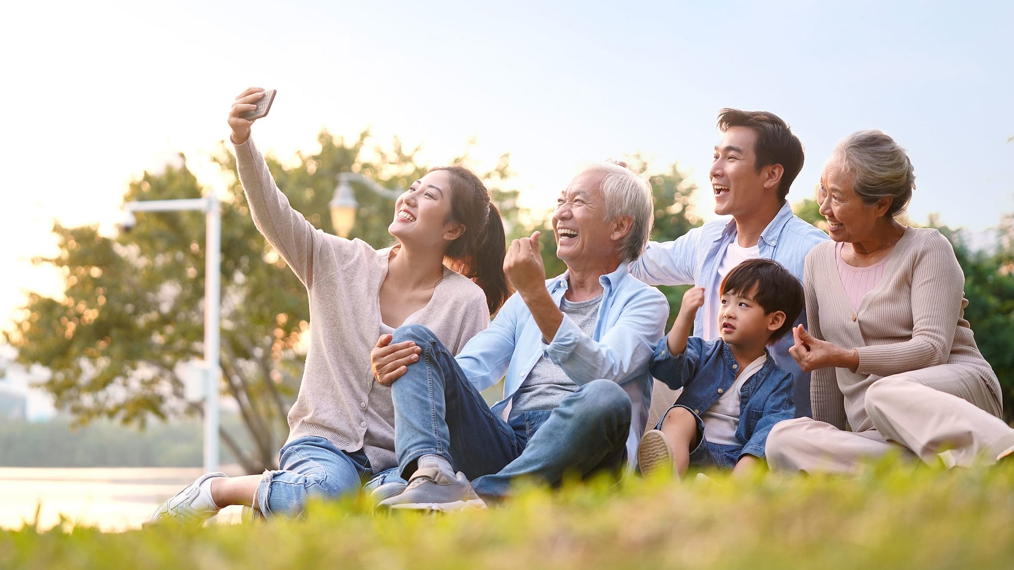 Multigenerational Asian family taking a selfie while sitting on the grass.