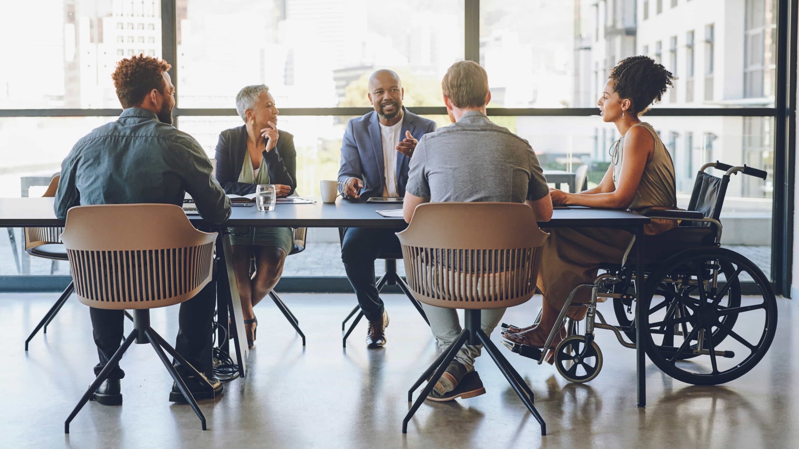 7-13 Blog Image diverse group of employees sitting and talking at conference room table