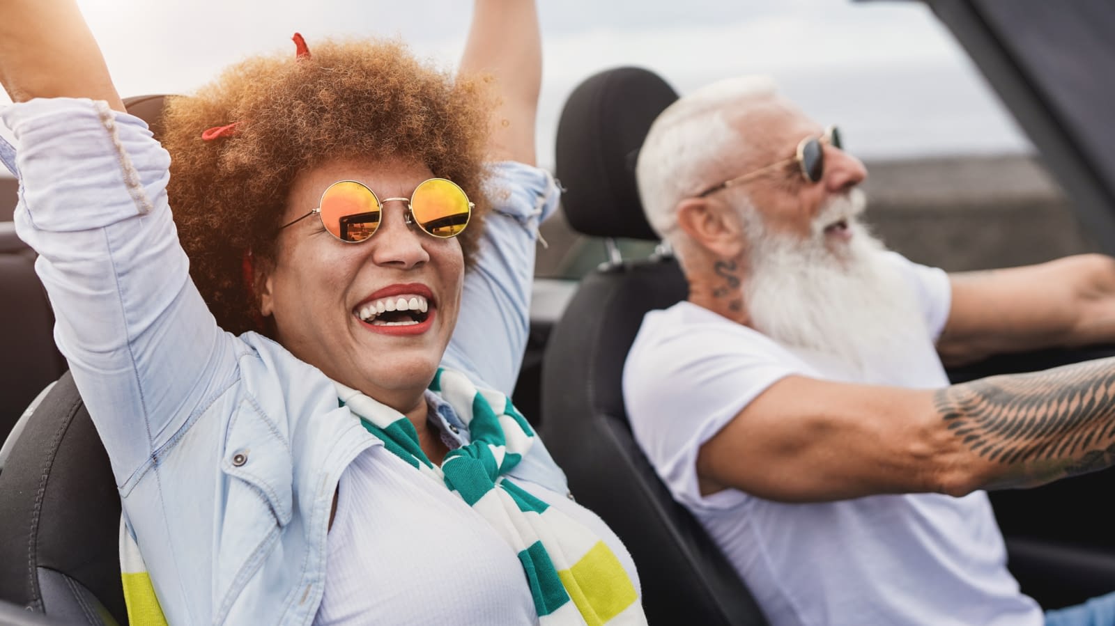 Trendy senior couple having fun inside convertible car – Multiracial mature people on a road trip with cabriolet car Senior Couple riding in car
