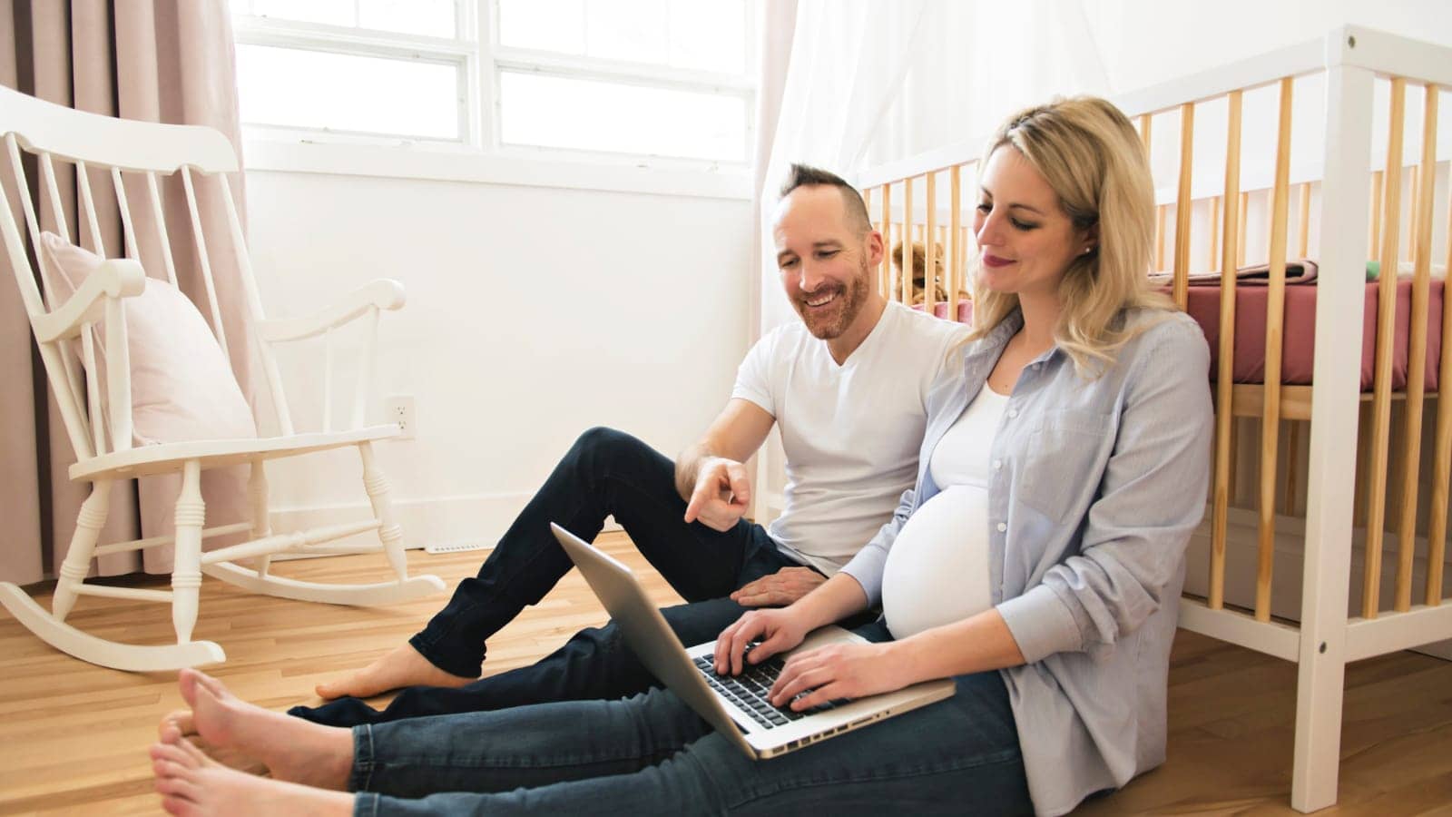 Pregnant couple in their nursery on a laptop