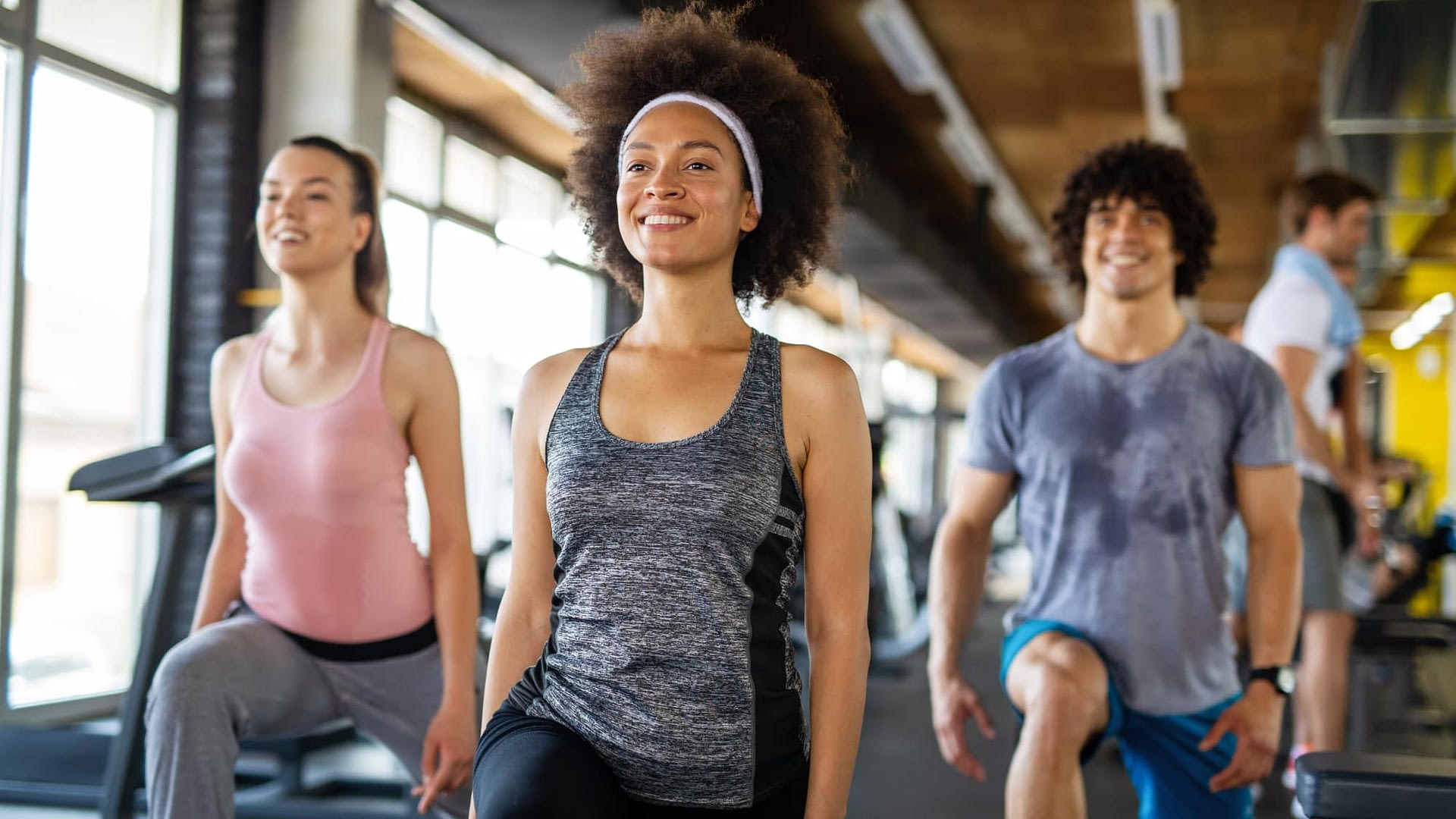 Multi-ethnic group of young adults doing lunges in unison at a gym / fitness center