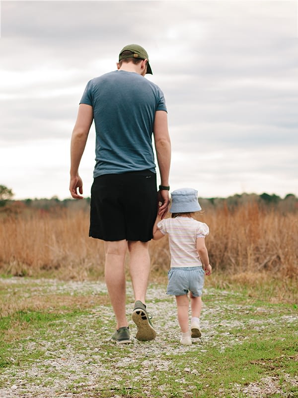 Father and young daughter walking through a field