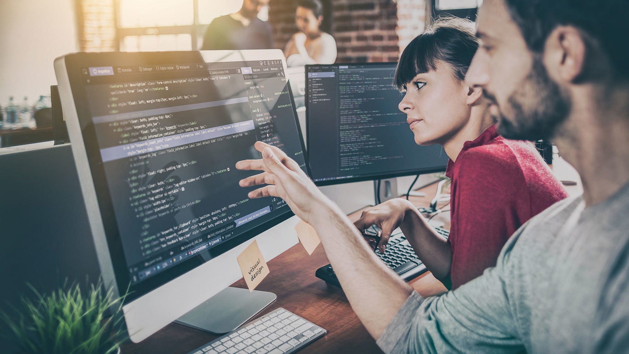 Two individuals looking at a computer screen displaying lines of code.