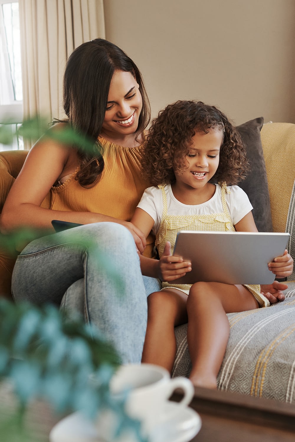 Shot of an attractive young woman and her daughter sitting on the sofa at home and using technology - stock photo