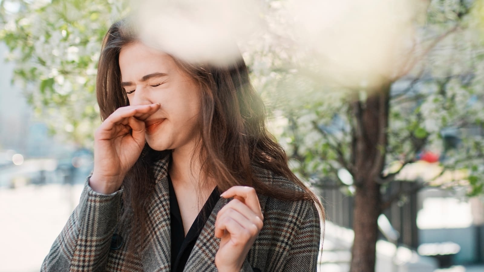 spring allergies women wiping her nose under a tree outside