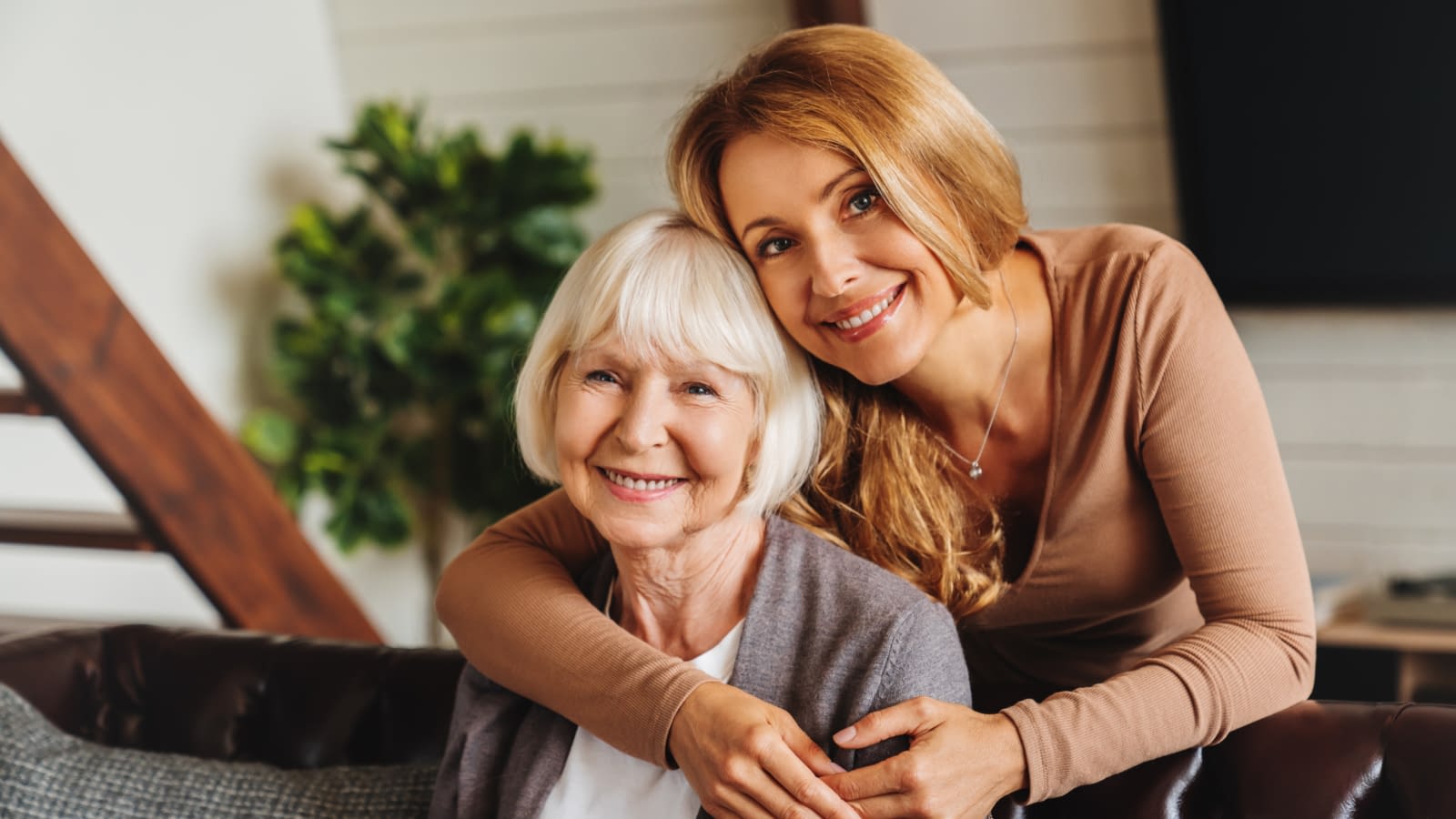 Cheerful middle aged woman embracing senior mother at home and looking at camera Middle aged woman and mom