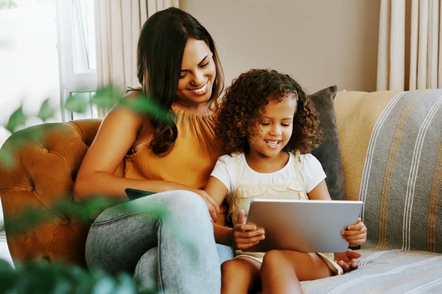 Young woman and her daughter sitting on the sofa at home and using technology