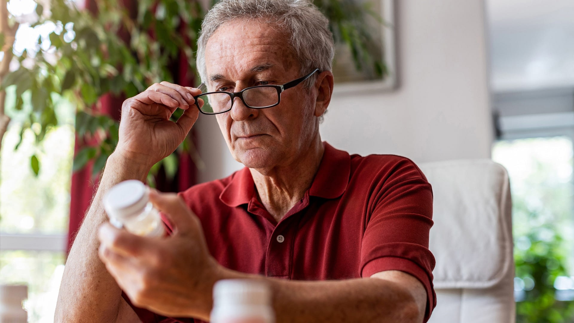 Senior man sitting at table reading the label on a prescription.