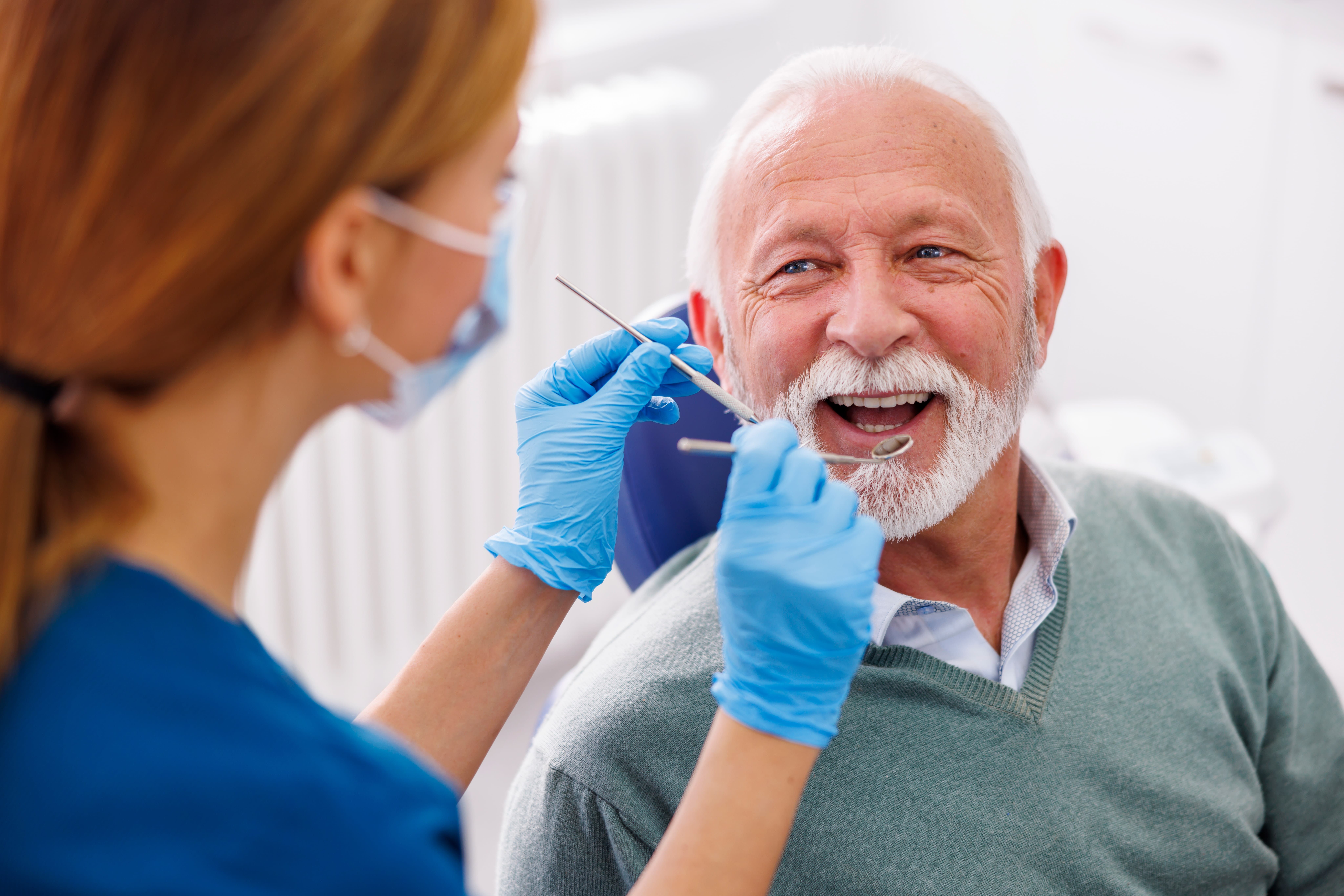 Doctor checking up patient's teeth at dentist office; senior man at dental checkup