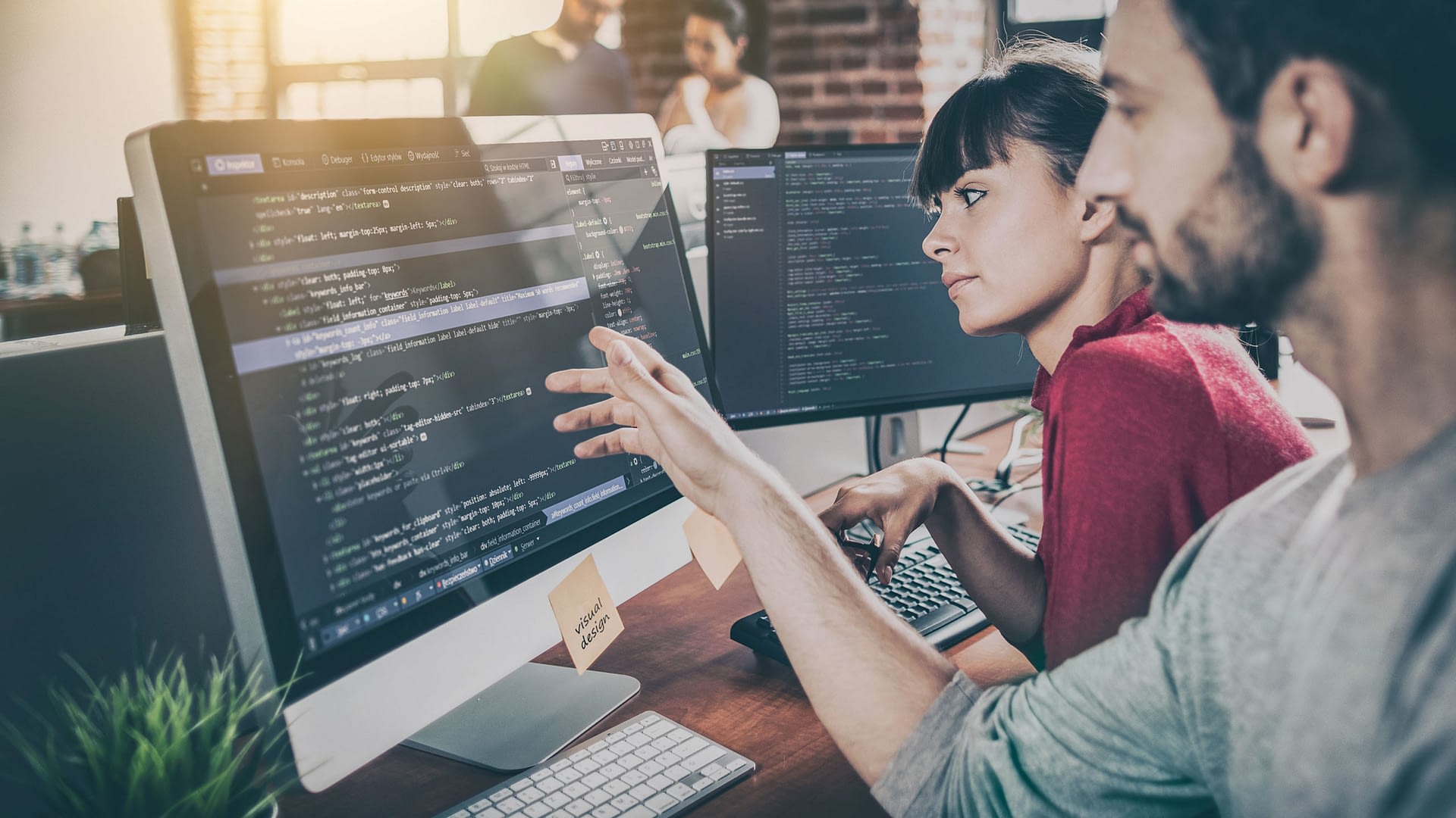 Two individuals looking at a computer screen displaying lines of code.