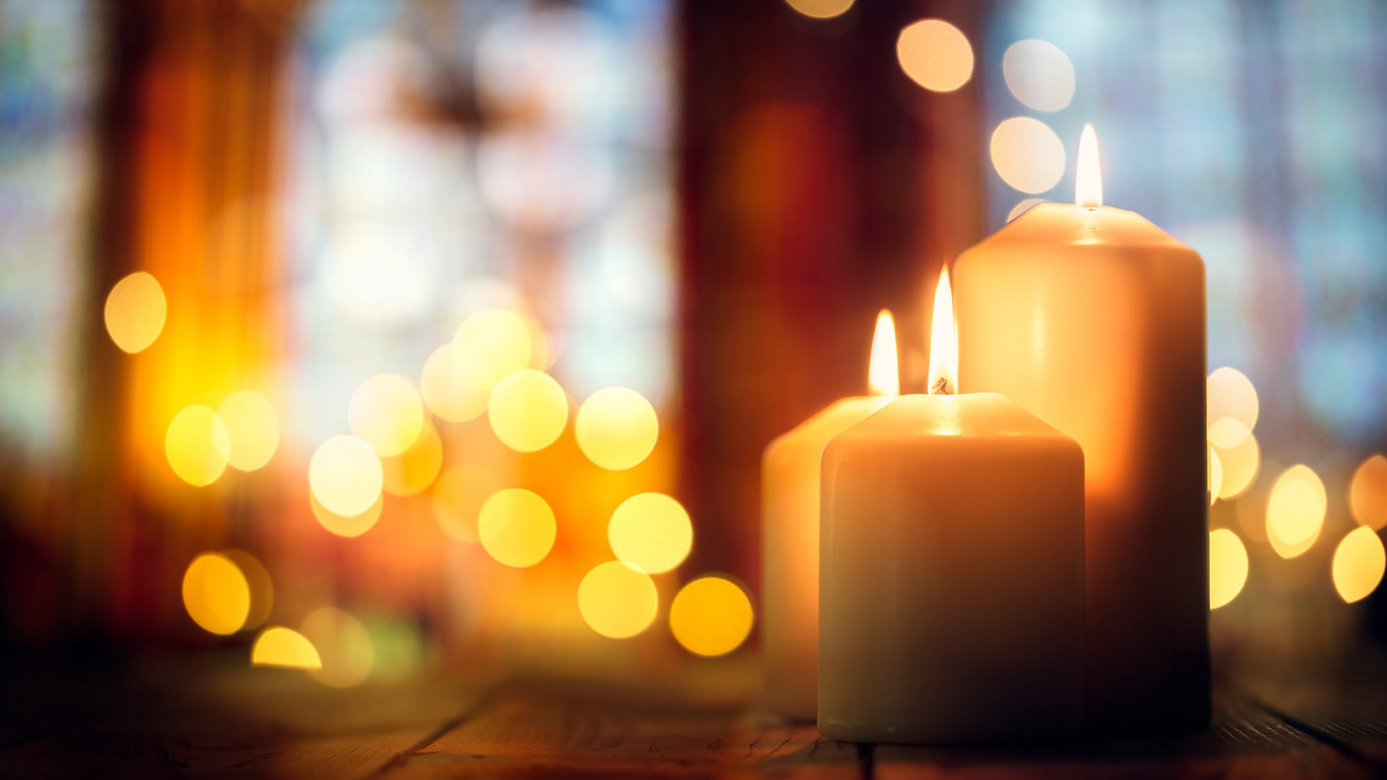 Close up of lit candles with large church windows in the background.