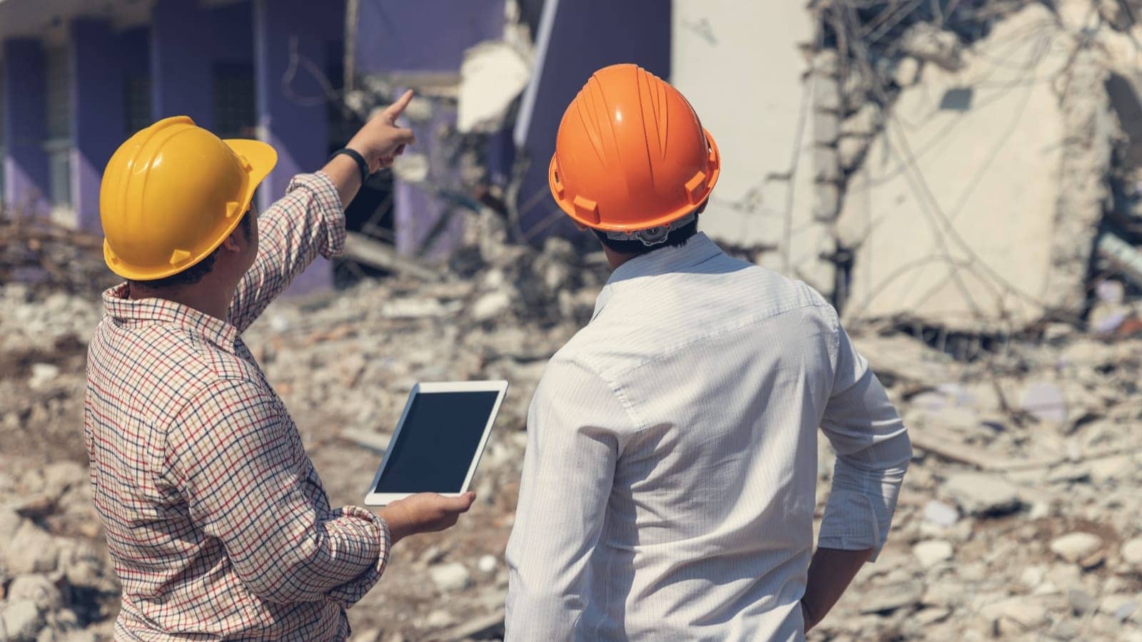 workers with hard hats and tablet assessing earthquake damage to a building