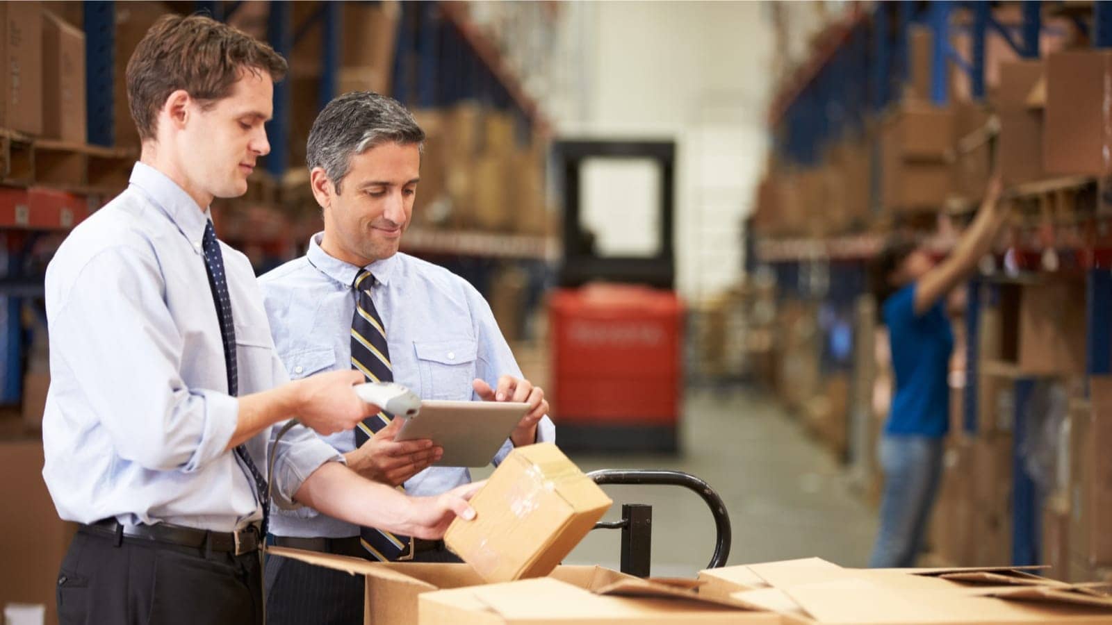 two coworkers in casual suits looking at packages in a warehouse