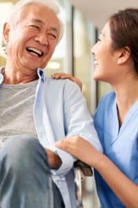 Nurse laughing with senior patient sitting in wheelchair.